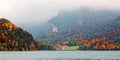 Lake Alpsee on a foggy autumn day with colorful foliage on lakeside mountains and New Swanstone Castle Schloss Neuschwanstein