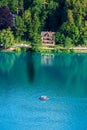 Lake Bled, Slovenia - Traditional Slovenian Pletna boat on Lake Bled with turquoise blue water, weekend house and forest