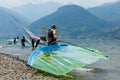 Lake Como, Italy - July 21, 2019. Man windsurfer carrying a sail into the mountain lake, surf board in the foreground
