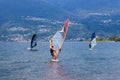 Lake Como, Italy - July 21, 2019. Water sport: group of three windsurfers surfing the wind on waves on a sunny summer day near the