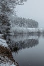 Lake covered with fresh snow.Winter pond,foggy cloudy landscape reflected in water,snowing day.White misty countryside snowy trees Royalty Free Stock Photo