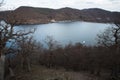 lake at the foot of a mountain surrounded by low mountains in autumn or winter surrounded by trees without leaves under Royalty Free Stock Photo