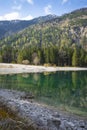 Lake at front of mountain with forest tree reflection and stone shore