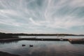 Lake landscape under a cloudy sky with two ducks swimming by a wooden pier Royalty Free Stock Photo