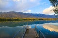 Lake in the mountains. Old wooden pier for fishing. Beautiful nature, reflection of clouds and mountains in blue water. Kyrgyzstan