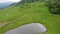 The lake in the mountains. Several SUVs are driving along a mountain road along a dirt road. Aerial view