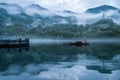 Lake with reflections and a small boat with foggy mountains on the background