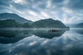 Lake with reflections and a small boat with foggy mountains on the background