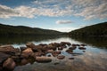 Lake with rocks in the foreground and reflection of sky and surrounding forest