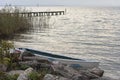 Lake shore with boat moored between large boulders. Background with water, wooden jetty and background sailboat.