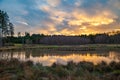 a lake surrounded by trees and grass under a cloudy sky with a sunset in the background and a forest in the foreground,