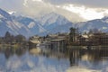 Lake view of houses and reflections in winter with snow capped mountains behind Royalty Free Stock Photo
