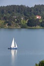 Lake view with a small blue sailboat with sail and hull reflection in the water