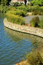 Lakeside cement wall with twisting and winding wall and sidewalk with shrubs and plants on outskirts of pond and water Royalty Free Stock Photo
