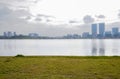 Lakeside grassy lawn with modern buildings in background on cloudy day