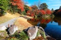 Lakeside gravel path leading into a forest of maple trees & the fiery foliage reflected in the peaceful water of the pond Royalty Free Stock Photo