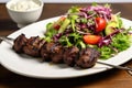 lamb kebabs on white plate, mixed salad on the side