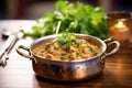 lamb korma in a brass pot, garnished with cilantro, on a wooden table