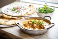 lamb korma in a ceramic dish, yogurt dollop, with naan on the side