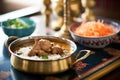 lamb korma in a copper serving dish, rice on copper plate nearby