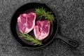 Lamb loin chops with rosemary in a cast iron frying pan. On black granite