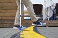 A lame man with an elbow crutch steps over a cable channel in the street.