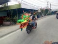 Lamongan, East Java, Indonesia. a motorcyclist carrying a kite in the shape of a green dragon's head