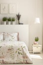 Lamp above cabinet next to bed with plants on headboard in feminine bedroom interior. Real photo Royalty Free Stock Photo