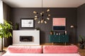 Lamp above pink couch in grey apartment interior with green cabinet and fireplace.