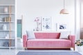 Lamp above pink settee with pillows in pastel living room interior with flowers and posters. Real photo