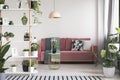 Lamp above table with flowers in front of red sofa in white living room interior with plants. Real photo Royalty Free Stock Photo