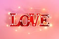 Lamp in the form of red letters love and garland on a pink background