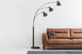 Lamp next to brown leather couch in interior with copy space on empty wall. Real photo Royalty Free Stock Photo