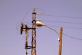 Lamp post anchored to a wooden telecommunication pole with a high voltage tower in the background