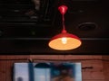 Lamp with a red lampshade under a dark ceiling. LED filament bulb. Photo through the glass of a cafe. Wood panels on the walls Royalty Free Stock Photo