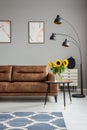 Lamp and table with sunflowers next to leather couch in grey flat interior with posters. Real photo Royalty Free Stock Photo