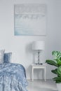Lamp on white cabinet next to blue bed in bedroom interior with posters and plant. Real photo Royalty Free Stock Photo