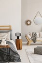 Lamp on wooden stool next to bed in apartment interior with pouf and candles on table Royalty Free Stock Photo