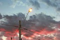 Lamppost with electric wires and a lighted lamp. In the background cloudy late afternoon sky Royalty Free Stock Photo