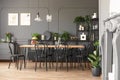 Lamps above wooden table and black chairs in grey dining room in