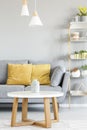 Lamps above wooden table in front of grey sofa with yellow pillo