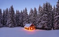 The lamps light up the house at the evening time. Winter landscape. Wooden hut on the lawn covered with snow. Mystical night.