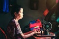 a mother who works as a seamstress is sitting in front of her sewing machine, a traditional Indonesian woman