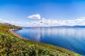 Blue sky with white puffy clouds over rocky coastal line and mountains in a distance Royalty Free Stock Photo