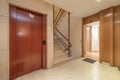 Landing of a residential building with elevators with red metal doors, stairs with cream-colored marble steps and entrances to