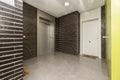 Landing of residential building with metal elevator, gray stoneware floors and black brick walls