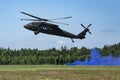 Landing of swedish military helicopter Blackhawk UH-60. Military armed men with smoke bomb near forest under blue sky