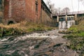 Landscape with Aleksupiti in the foreground and Aleksupite waterfall in the distance, as well as an old red brick industrial