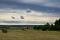 Landscape, bales of hay on a beveled empty field with perpective in the distance in cloudy weather in the sky gray storm clouds Royalty Free Stock Photo
