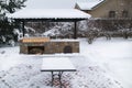 Landscape with barbeque area, snowbanks of white snow, pine trees in country garden.